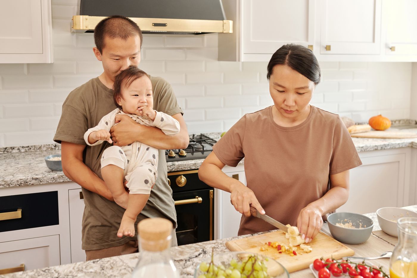 爸爸抱着嬰兒,媽媽在廚房準備食物